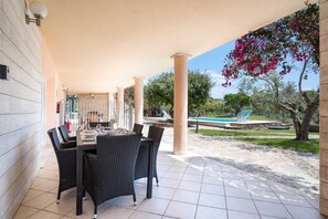 Une terrasse extérieure avec une table et des chaises, une piscine et un espace abrité avec des colonnes.