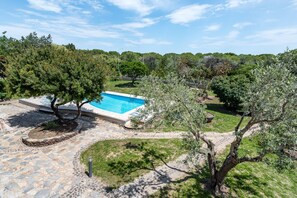 Una piscina rodeada de baldosas de piedra, árboles y un sendero de piedra.