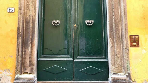 A green double door with ornate metal handles, set within a stone archway, against a yellow wall. - Apartment 'Federico - In Pieno Centro' with Wi-Fi and Air Conditioning (Lucca)