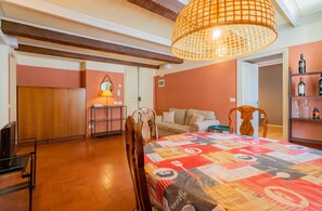 A cozy room with a wooden ceiling, a dining table with a patterned tablecloth, a sofa, and a television. - Apartment 'Federico - In Pieno Centro' with Wi-Fi and Air Conditioning (Lucca)