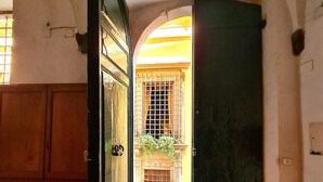 An open doorway leading to a courtyard with a tiled floor, a metal gate, and a building with yellow walls and a window with bars. - Apartment 'Federico - In Pieno Centro' with Wi-Fi and Air Conditioning (Lucca)