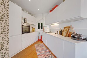 Una cocina moderna con armarios blancos, horno empotrado y un extintor de incendios rojo.