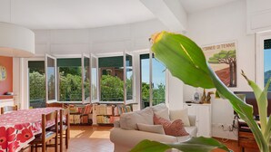 A living room with a dining table, sofa, and a large window with a view of greenery.