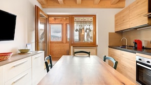 A kitchen with wooden cabinets, a dining table, chairs, a TV, and a window with curtains.