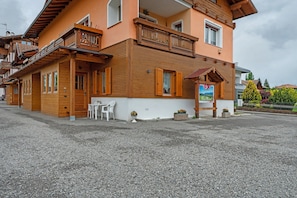 A two-story building with wooden balconies, a small outdoor seating area, and a gravel driveway. - Apartment 'Piano Terra 3' with Mountain View, Private Terrace and Wi-Fi (Romeno)
