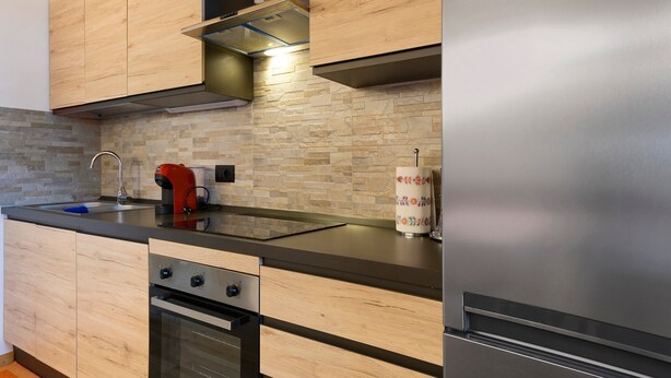 A modern kitchen with wooden cabinets, a stainless steel range, and a built-in oven. - Apartment 'Piano Terra 3' with Mountain View, Private Terrace and Wi-Fi (Romeno)