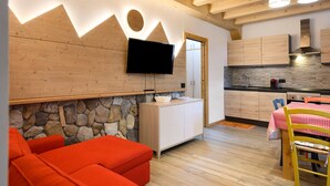 A modern kitchen with a stone wall, wooden cabinets, and a flat-screen TV mounted above a counter. - Apartment 'Piano Terra 3' with Mountain View, Private Terrace and Wi-Fi (Romeno)