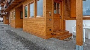A wooden cabin with large windows, a wooden door, and a set of stairs leading to a porch. - Apartment 'Piano Terra 3' with Mountain View, Private Terrace and Wi-Fi (Romeno)