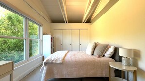 A bedroom with a large window, a bed with a quilt, a bedside table with a lamp, and a wardrobe. - Storybook Summer Stay - 4-bedroom house in charming Mill Valley (Mill Valley)