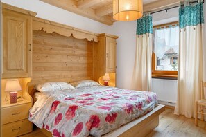 Une chambre à coucher en bois, avec un lit, des tables de chevet et une fenêtre avec des rideaux.
