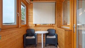 Una habitación pequeña con paredes de madera, una mesa redonda, dos sillas de mimbre y un ventanal.
