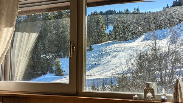 Une cabane en bois dotée d’une grande fenêtre donnant sur un paysage enneigé.