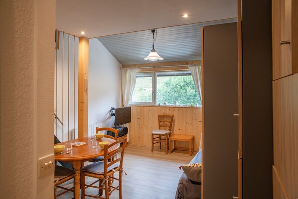 A compact room with a dining table, chairs, a television, and a window with curtains.