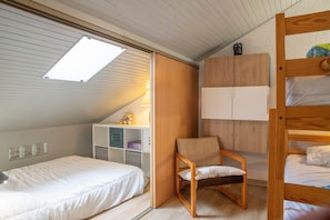A bedroom with a bunk bed, a single bed, a chair, a wardrobe, and a skylight.