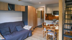 Un espace de vie compact comprenant un canapé, une table à manger, des chaises, un coin cuisine et un escalier.