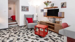 Ein Wohnzimmer mit Sesseln in Karomuster, einem roten Beistelltisch, einem Flachbildfernseher und einem Wandregal mit Dekoration.