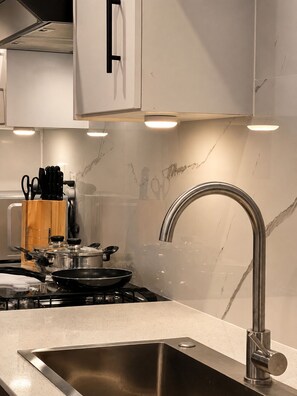 Una cocina moderna con un lavamanos de acero inoxidable, una estufa a gas y un protector contra salpicaduras de mármol.