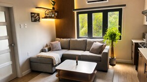 Una sala de estar moderna con un sofá seccional, una mesa de centro, una planta en maceta y una zona de cocina con estufa.