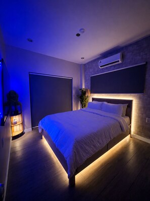 A modern bedroom with a large bed, a wall-mounted air conditioner, and a ceiling light fixture.