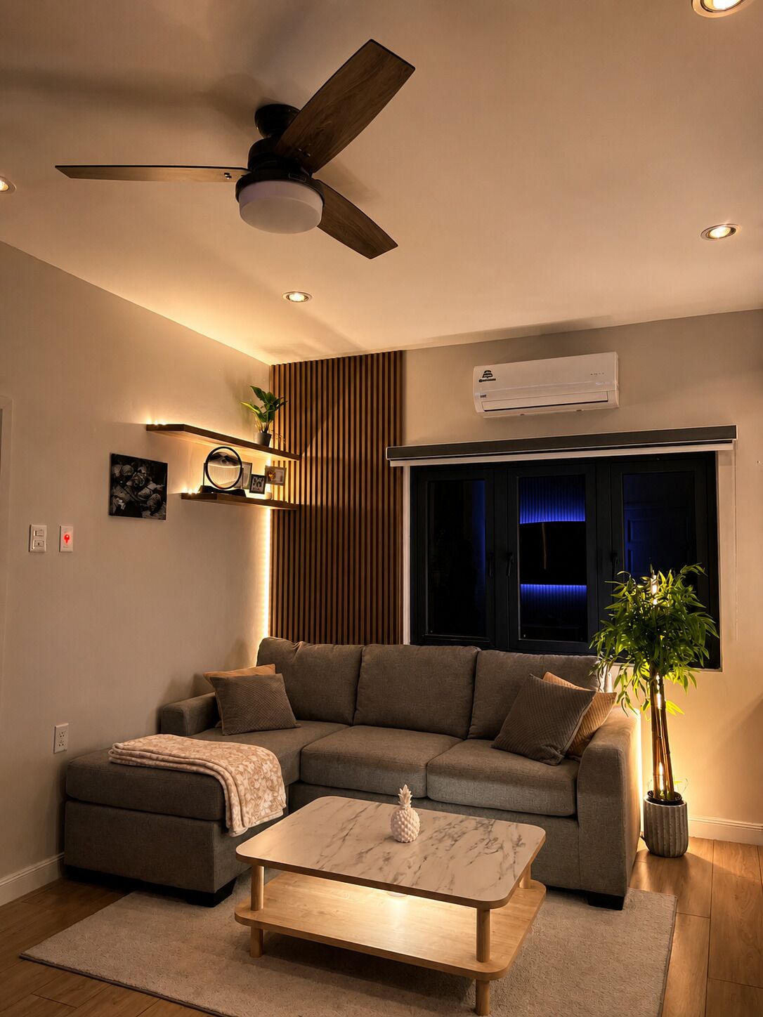 Una sala de estar moderna con un sofá modular, una mesa de centro de mármol, un ventilador de techo y un equipo de aire acondicionado.