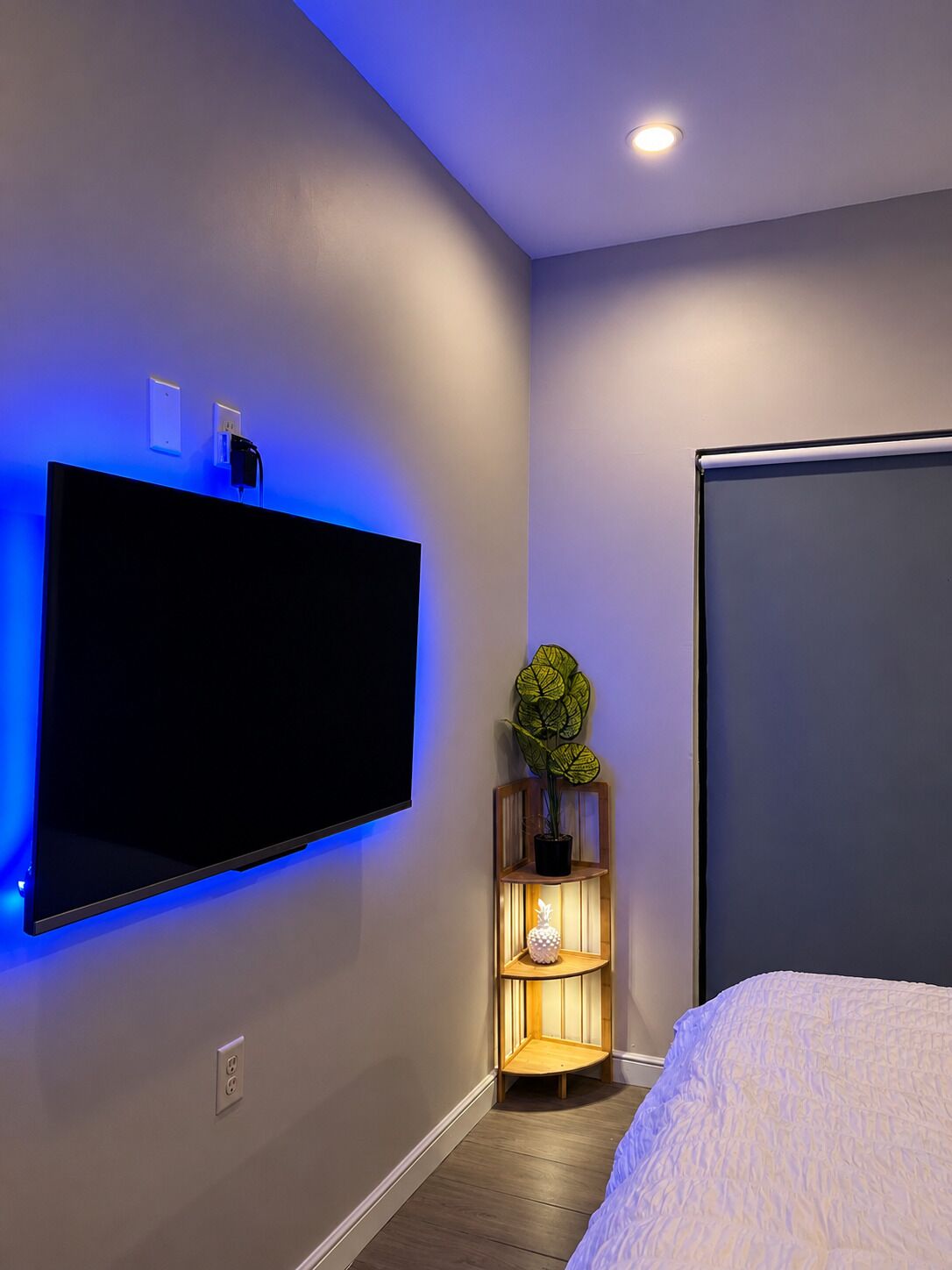 Et moderne soveværelse med et fladskærms-tv på væggen, et sengebord med en lampe og en seng med et hvidt dynebetræk.
