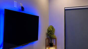 Et moderne soveværelse med et fladskærms-tv på væggen, et sengebord med en lampe og en seng med et hvidt dynebetræk.