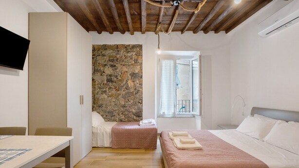 Un dormitorio con pared de piedra, una cama con colcha rosa, una mesita de noche y un televisor montado en la pared.