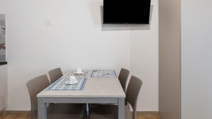 Un comedor con una mesa, sillas, un televisor de pantalla plana montado en la pared y un mantel estampado.