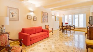 A living room with a red sofa, wooden chairs, a dining table with chairs, and a TV on a wooden cabinet. - Apartment 'La Chiocciola Nel Labirinto' with Balcony, Wi-Fi and Air Conditioning (Lucca)
