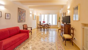 A living room with a red sofa, a dining table with chairs, a TV, and a radiator. - Apartment 'La Chiocciola Nel Labirinto' with Balcony, Wi-Fi and Air Conditioning (Lucca)