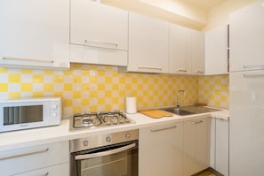 Uma cozinha com armários brancos, micro-ondas, fogão a gás, pia e painel de fundo xadrez amarelo e branco.