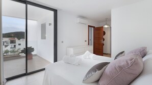 Ein modernes Schlafzimmer mit einem großen Schiebeglastür, die auf einen Balkon führt, einem Bett mit Kissen, einem Nachttisch und einer Klimaanlage.