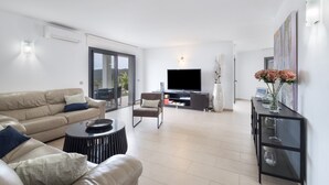 Ein modernes Wohnzimmer mit Sofa, Sessel, Couchtisch, Flachbildfernseher und einer Konsole mit einer Vase.