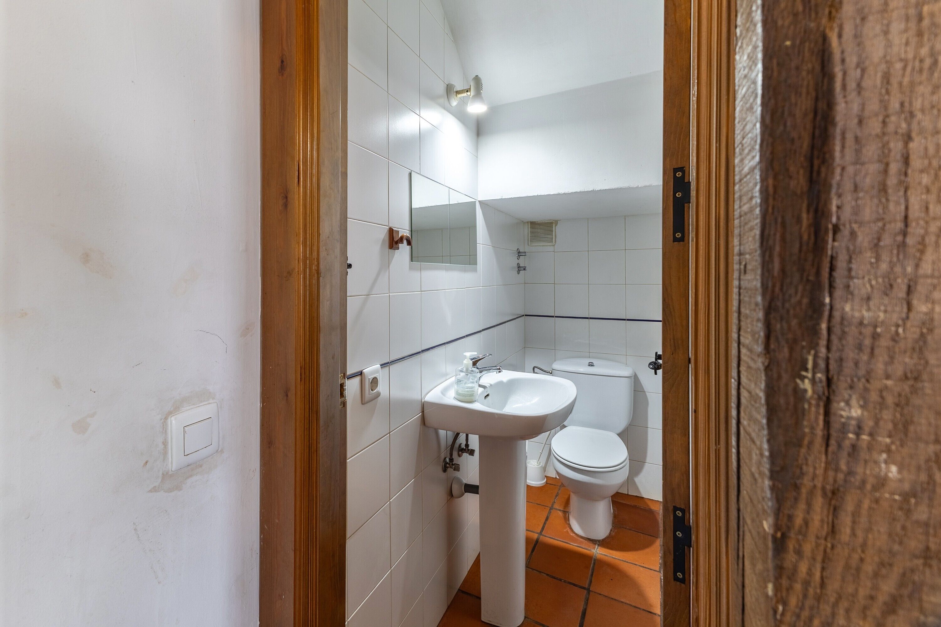 Une salle de bain avec des carreaux blancs, un lavabo sur colonne, des toilettes et un miroir.