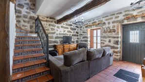 Una habitación con paredes de piedra, un sofá, un televisor y una escalera con baldosas estampadas.