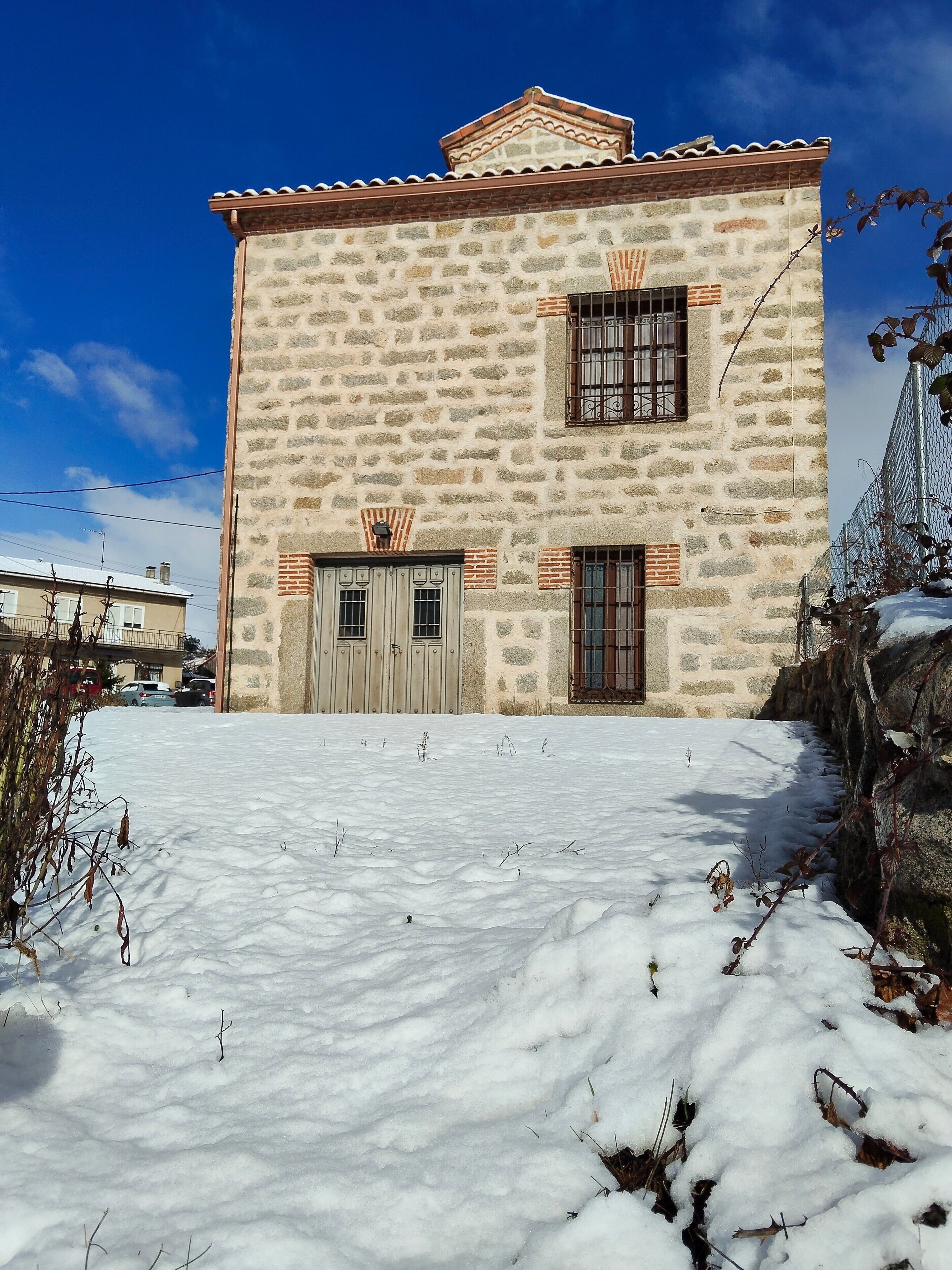 Un edificio de piedra con techo de tejas, dos puertas y ventanas con rejas.