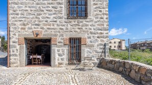 Un edificio de piedra con un patio adoquinado, una mesa y sillas de madera afuera y una ventana con barrotes.