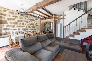 Une pièce avec un mur en pierre, un escalier en bois, un canapé et une table à manger.