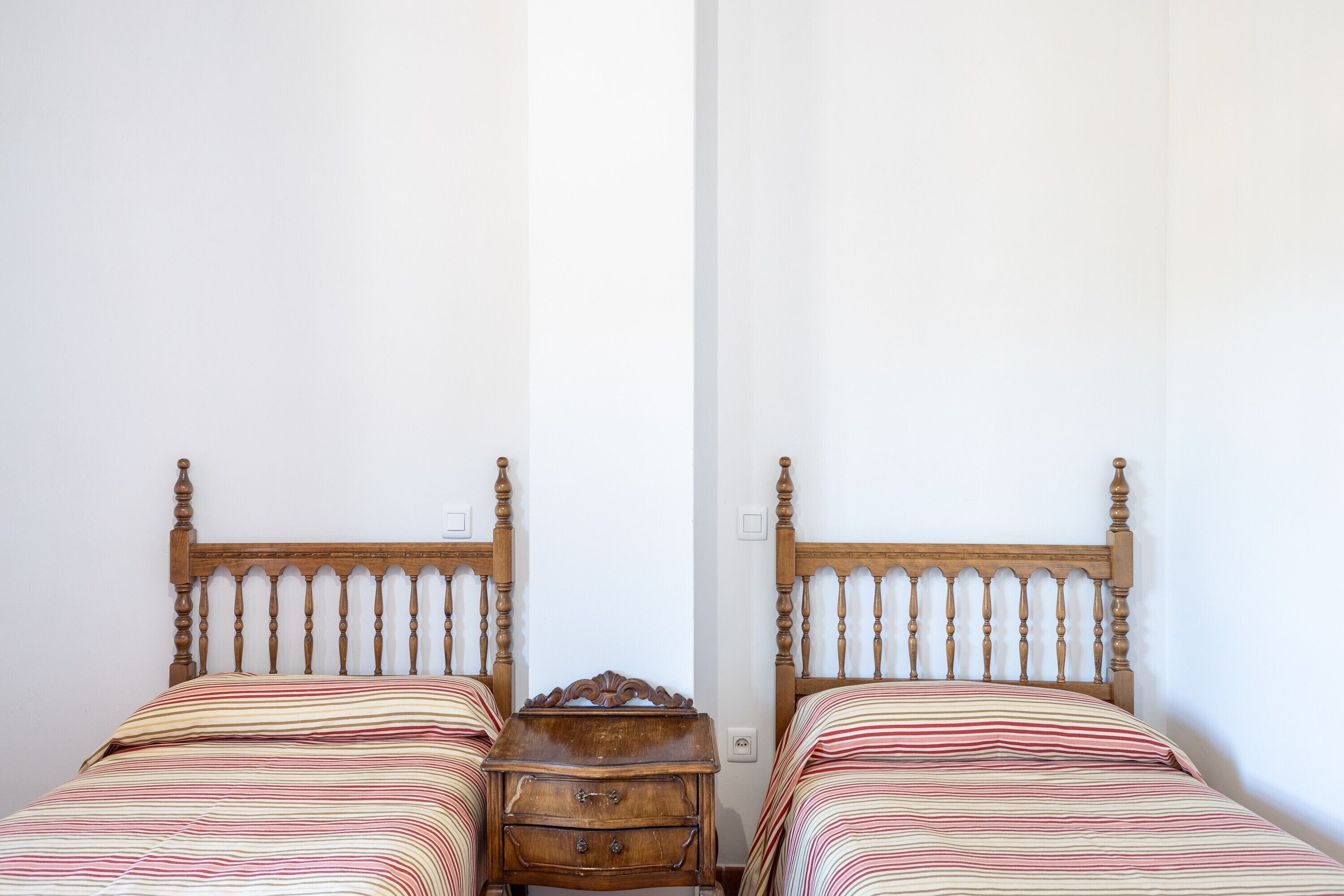 Dos camas individuales con cabeceros de madera, mesitas de noche de madera y una pared blanca lisa.