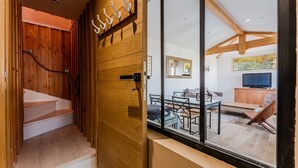 Un escalier en bois mène à une pièce comprenant un coin repas, un téléviseur et offrant une vue sur l’extérieur.