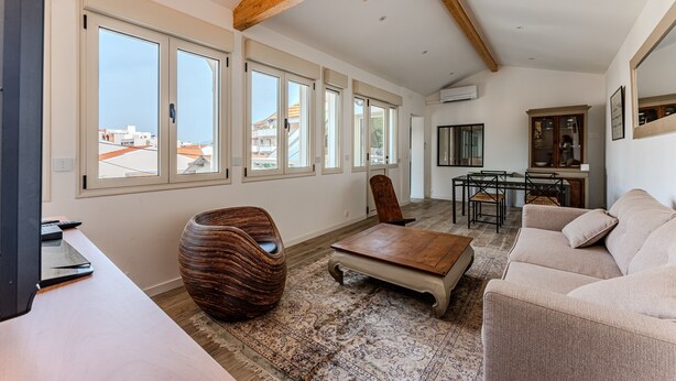 Un vaste espace de vie doté de grandes fenêtres, d’un plafond en bois, d’un canapé, d’une table basse et d’un coin repas.