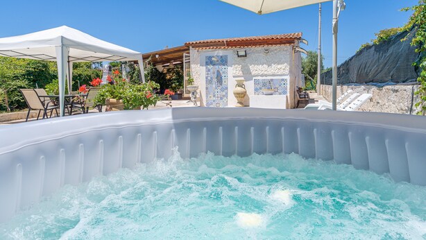 Jacuzzi con pared de azulejos al fondo, zona de estar techada y pared de piedra con puerta de azulejos.