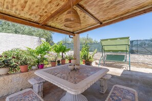 Eine Terrass mit Tisch und Stühlen, umgeben von Topfpflanzen und einem grünen Stuhl.
