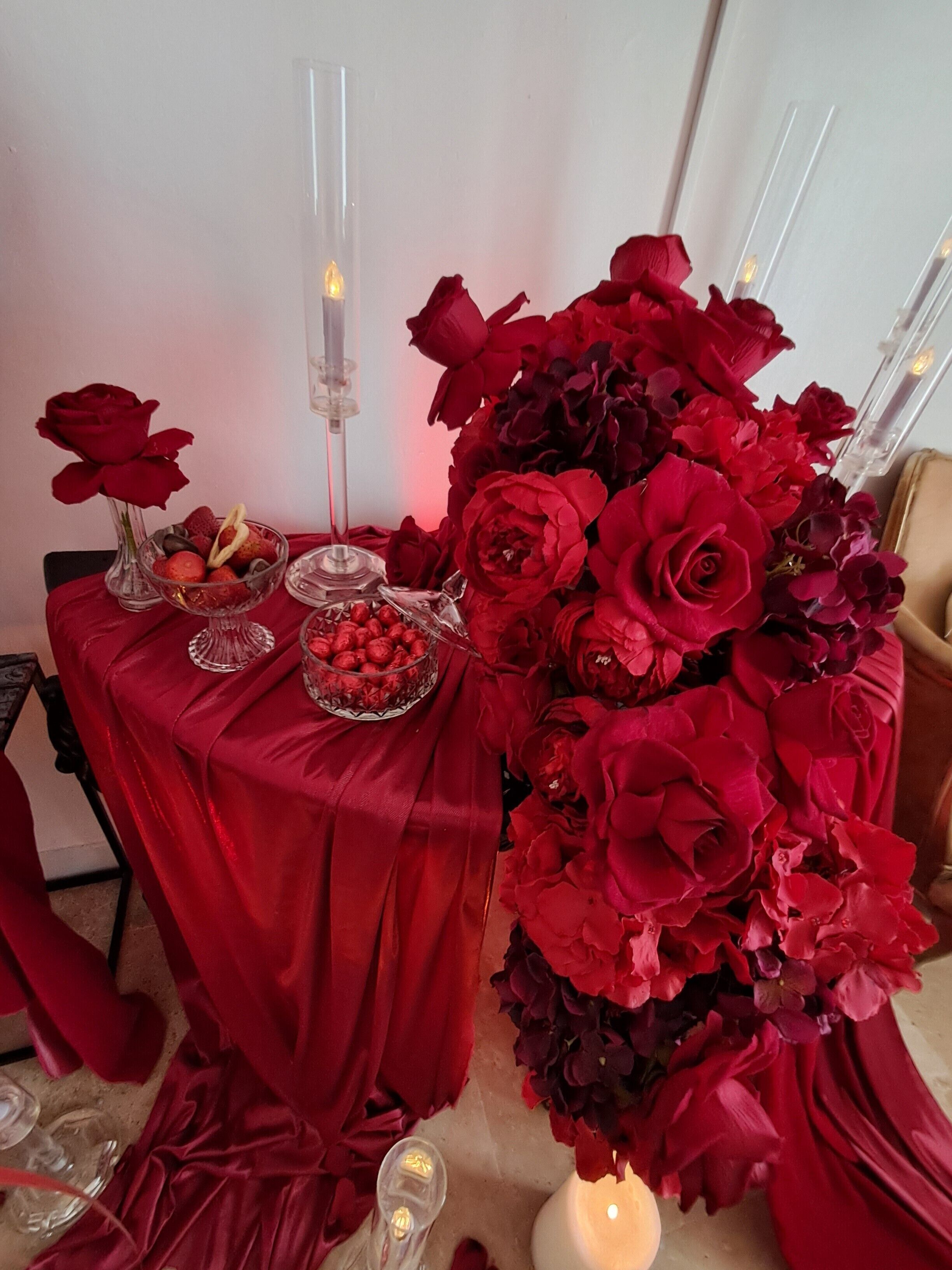 Ein Tisch mit rotem Tischtuch, Kerzen, einer Vase mit roten Rosen und einer Schüssel mit roten Beeren.