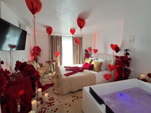Una habitación con cama, televisión, bañera y detalles en rojo.