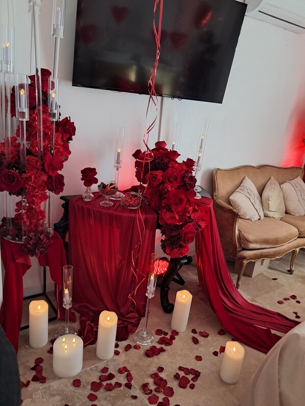 A room with a red draped table, candles, and rose petals on the floor.