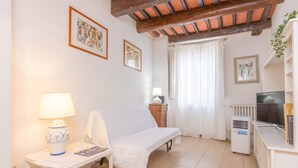 Una habitación con una cama, un escritorio con lámpara, un radiador, un televisor y cuadros en las paredes.