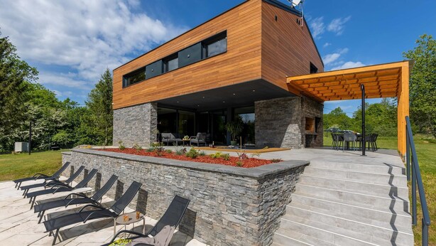 A modern two-story house with a wooden exterior, stone accents, and a covered outdoor seating area with lounge chairs. - Amazing home in Slunj (Slunj)