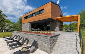A modern two-story house with a wooden exterior, stone accents, and a covered outdoor seating area with lounge chairs. - Amazing home in Slunj (Slunj)
