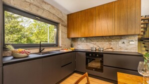 A modern kitchen with dark cabinets, a marble backsplash, and a window overlooking greenery. - Amazing home in Slunj (Slunj)